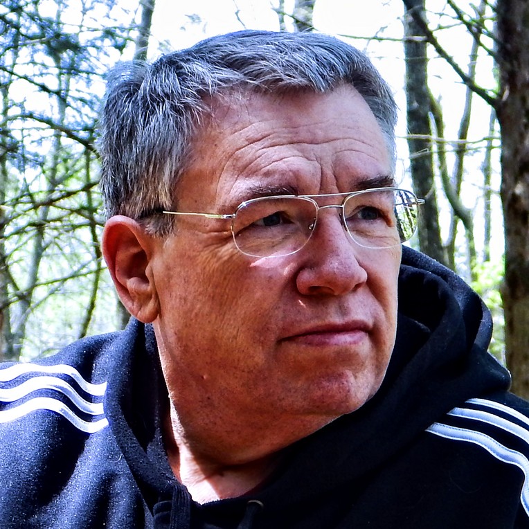 A man wearing glasses and a black hoodie in the woods.