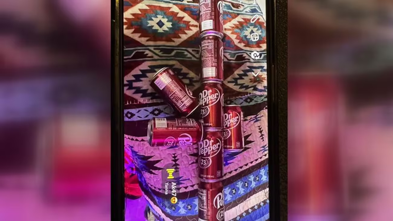 Several Dr. Pepper cans arranged in the shape of a rifle on a patterned blanket.